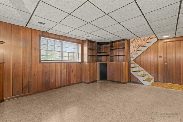 basement featuring a paneled ceiling and wooden walls