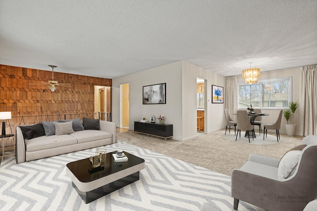 carpeted living room featuring ceiling fan with notable chandelier, a textured ceiling, and wooden walls