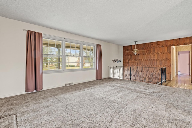 carpeted empty room featuring wooden walls, ceiling fan, and a textured ceiling