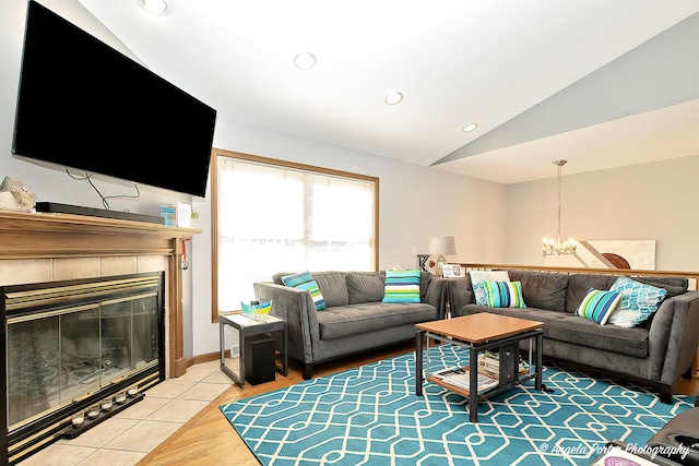 living room with hardwood / wood-style flooring, a notable chandelier, lofted ceiling, and a tiled fireplace