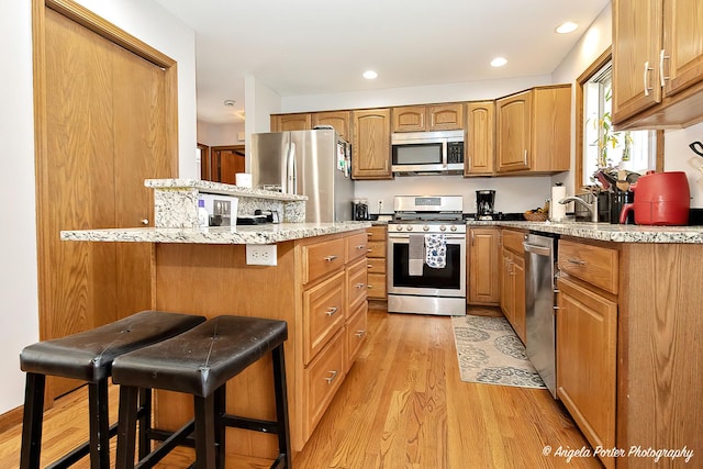 kitchen with sink, a kitchen bar, stainless steel appliances, and light hardwood / wood-style flooring