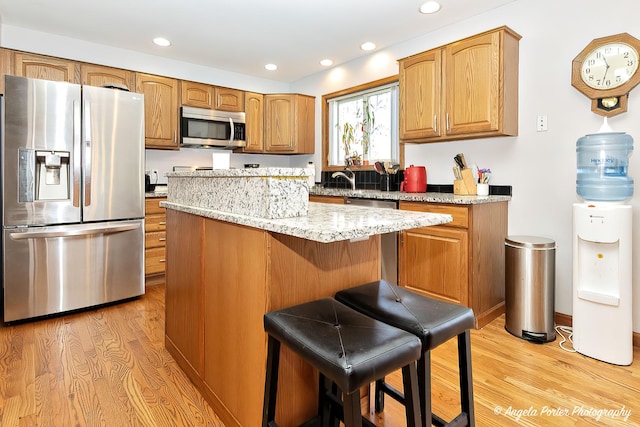 kitchen featuring light stone countertops, light wood-type flooring, a kitchen island, a kitchen bar, and stainless steel appliances