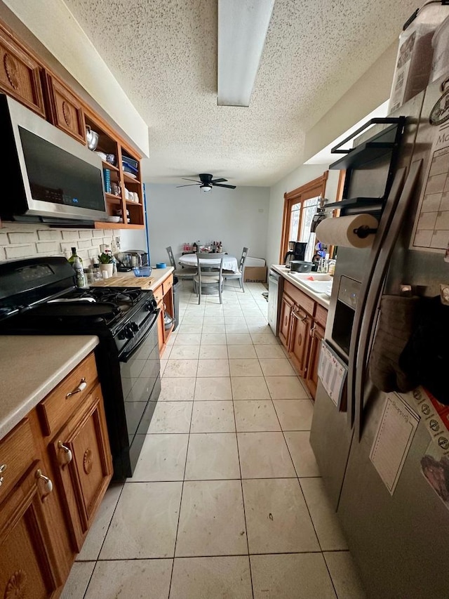 kitchen featuring backsplash, ceiling fan, light tile patterned floors, a textured ceiling, and appliances with stainless steel finishes