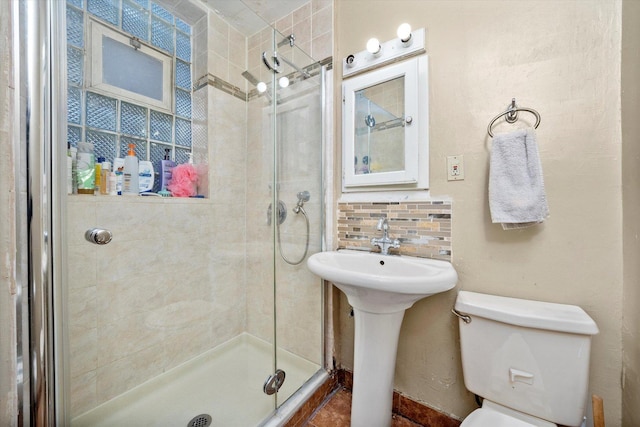 bathroom featuring sink, toilet, a shower with door, and backsplash