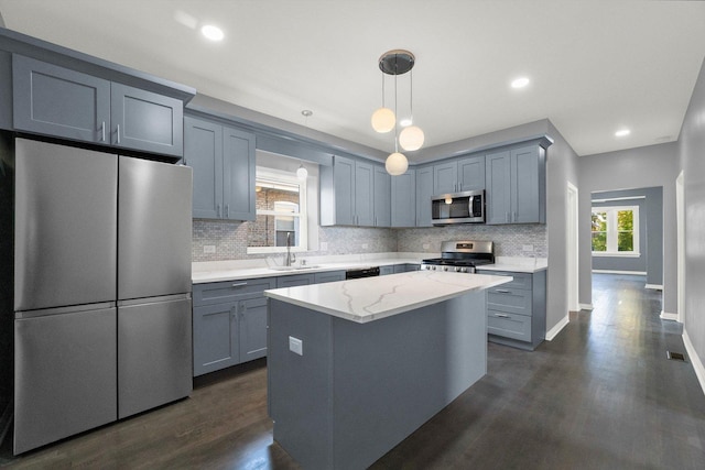 kitchen featuring a center island, sink, hanging light fixtures, appliances with stainless steel finishes, and light stone counters