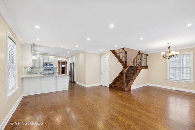 unfurnished living room featuring sink, wood-type flooring, a chandelier, and ornamental molding