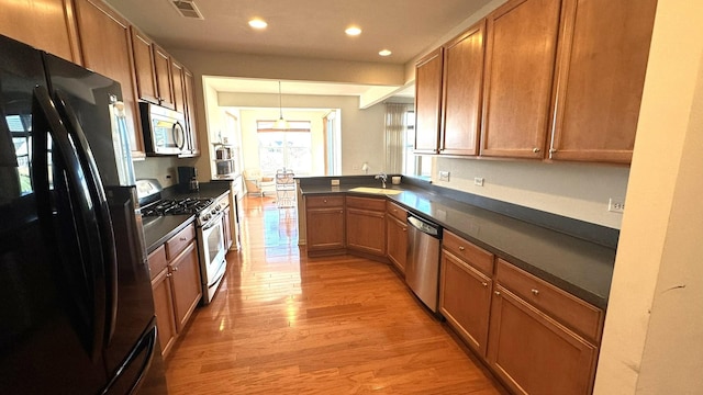 kitchen with hanging light fixtures, sink, appliances with stainless steel finishes, light hardwood / wood-style floors, and kitchen peninsula