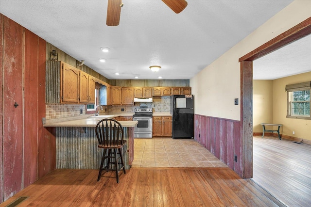 kitchen featuring kitchen peninsula, decorative backsplash, black fridge, stainless steel electric stove, and sink