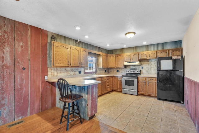 kitchen with kitchen peninsula, a kitchen breakfast bar, black fridge, stainless steel range with electric stovetop, and sink