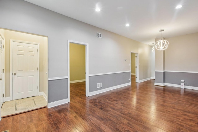 empty room with a notable chandelier and dark wood-type flooring