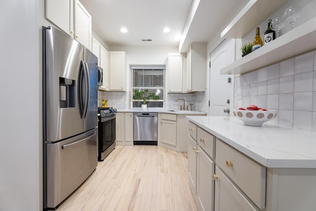 kitchen with sink, white cabinetry, appliances with stainless steel finishes, light hardwood / wood-style floors, and backsplash