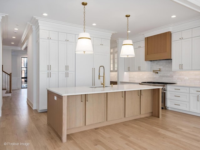 kitchen with white cabinetry, sink, high end stove, an island with sink, and light wood-type flooring