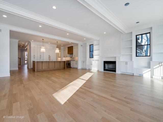 unfurnished living room featuring built in shelves, crown molding, sink, and light hardwood / wood-style floors