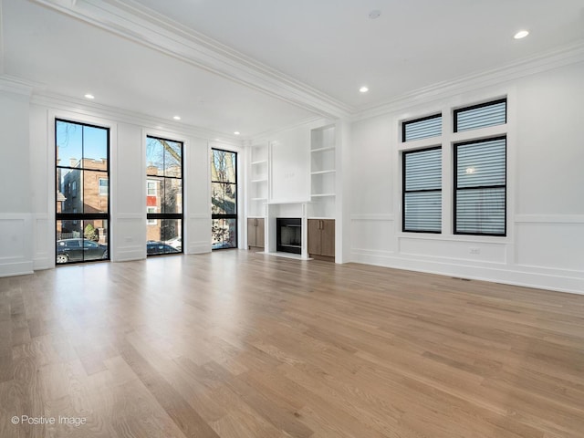 unfurnished living room with built in shelves, light wood-type flooring, and ornamental molding