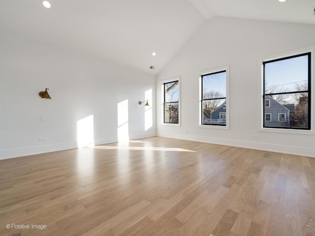 empty room featuring high vaulted ceiling, a healthy amount of sunlight, and light hardwood / wood-style floors