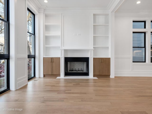 unfurnished living room featuring built in shelves, ornamental molding, and light hardwood / wood-style flooring