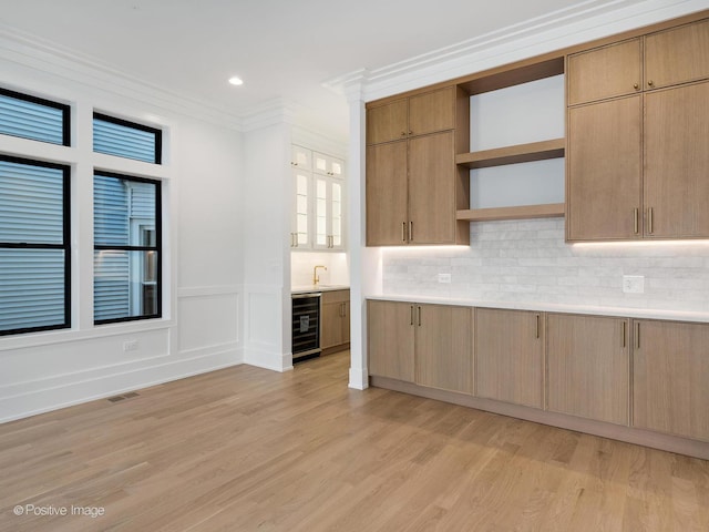 kitchen featuring wine cooler, crown molding, light hardwood / wood-style floors, decorative backsplash, and light brown cabinetry