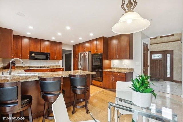 kitchen with light stone counters, a breakfast bar, a peninsula, black appliances, and a sink