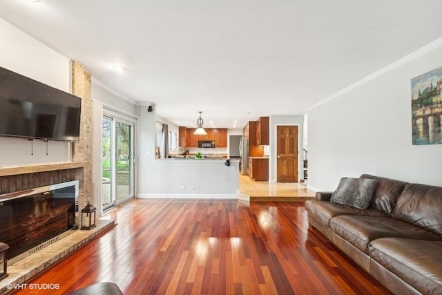 living area featuring a large fireplace, baseboards, crown molding, and hardwood / wood-style floors