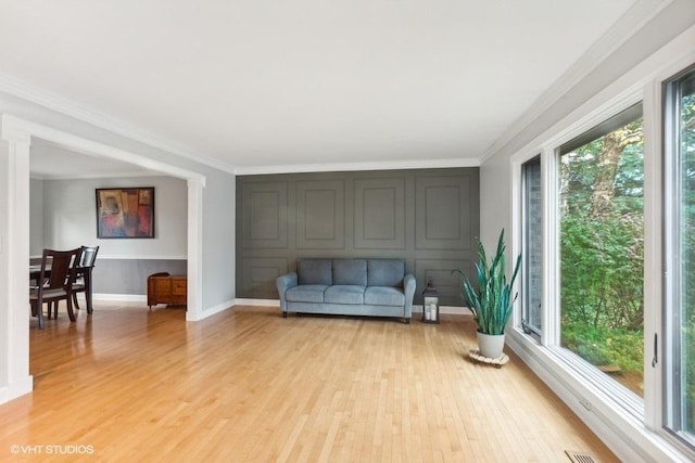 living area with ornamental molding, light wood-type flooring, and baseboards