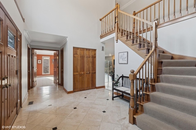 entrance foyer featuring light tile patterned floors, a towering ceiling, baseboards, stairway, and crown molding