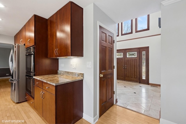 kitchen with stone counters, light wood finished floors, dobule oven black, freestanding refrigerator, and baseboards