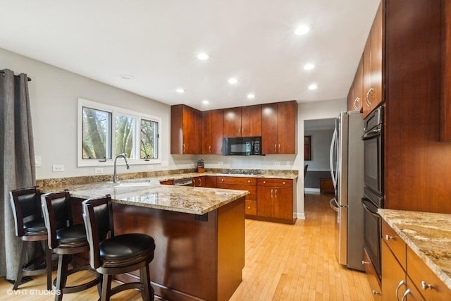 kitchen featuring black microwave, light stone counters, gas cooktop, a peninsula, and a sink