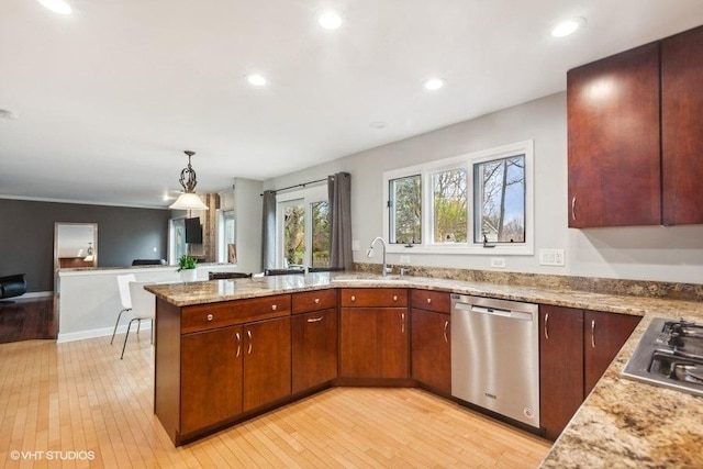 kitchen featuring light wood-style flooring, appliances with stainless steel finishes, open floor plan, a sink, and light stone countertops