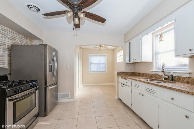 kitchen with sink, stainless steel gas range, light tile patterned flooring, dark stone counters, and white cabinets