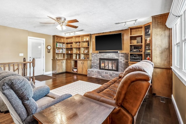 living room featuring a textured ceiling, dark hardwood / wood-style flooring, a brick fireplace, and built in features