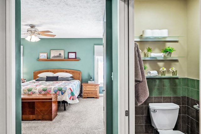 carpeted bedroom with a textured ceiling, ceiling fan, and tile walls