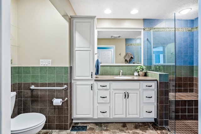 bathroom with toilet, vanity, tile walls, and tiled shower