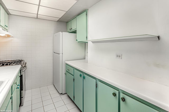 kitchen with gas stove, light tile patterned floors, tile walls, white fridge, and green cabinets