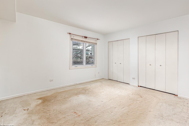 unfurnished bedroom featuring light colored carpet and two closets