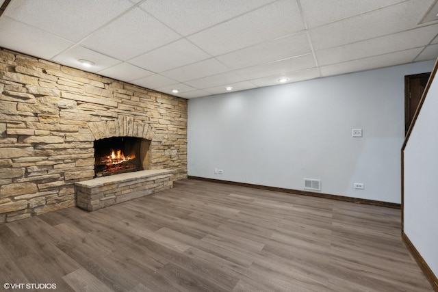 basement featuring a stone fireplace, a paneled ceiling, and hardwood / wood-style flooring