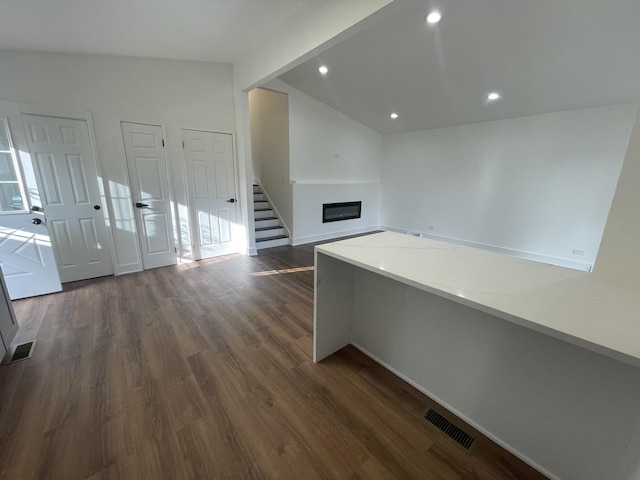 interior space featuring dark hardwood / wood-style flooring, vaulted ceiling, and light stone counters