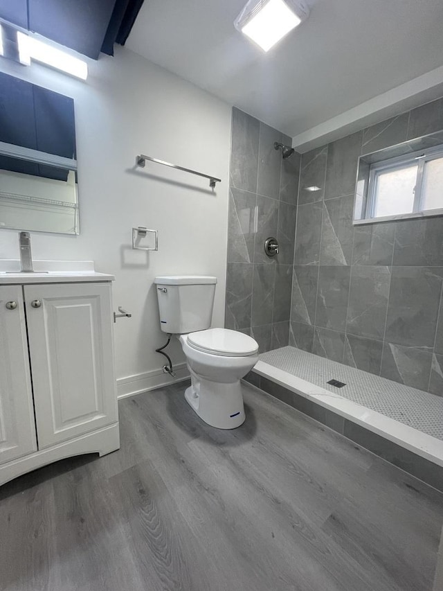 bathroom with tiled shower, hardwood / wood-style floors, vanity, and toilet