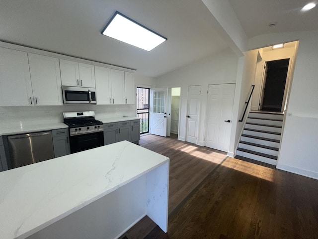 kitchen featuring lofted ceiling, dark hardwood / wood-style floors, decorative backsplash, appliances with stainless steel finishes, and white cabinetry