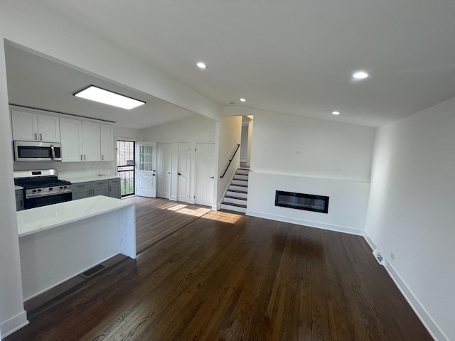 kitchen with appliances with stainless steel finishes, tasteful backsplash, vaulted ceiling, dark wood-type flooring, and white cabinetry