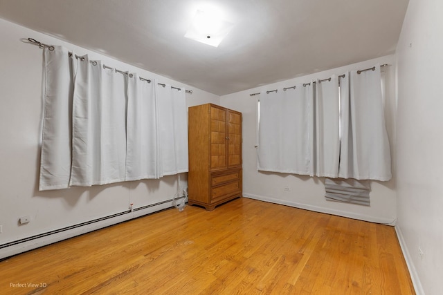 unfurnished bedroom with baseboard heating and light hardwood / wood-style floors