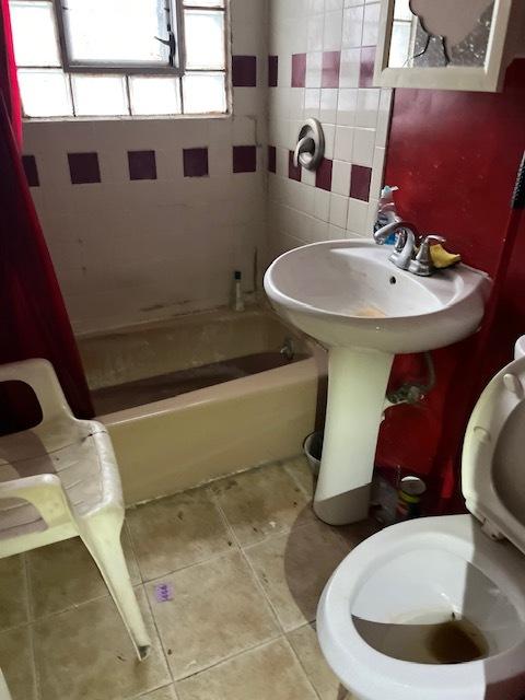 bathroom with shower / bath combo with shower curtain, tile patterned flooring, tile walls, and toilet