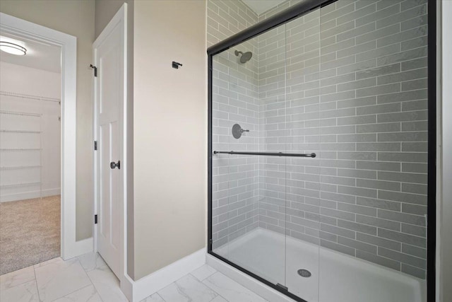 bathroom featuring marble finish floor, baseboards, a walk in closet, and a stall shower