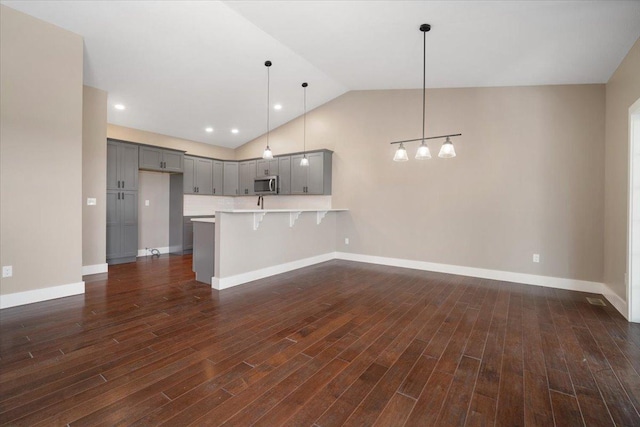 kitchen with stainless steel microwave, hanging light fixtures, a peninsula, light countertops, and a kitchen bar