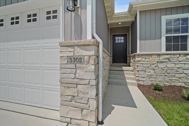 view of exterior entry featuring board and batten siding, stone siding, and a garage