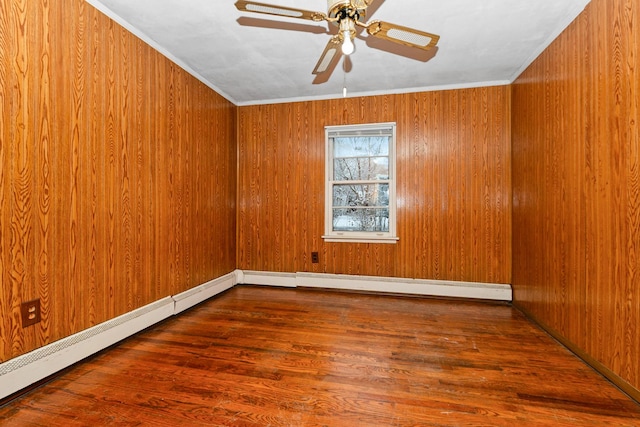 spare room with baseboard heating, crown molding, ceiling fan, wooden walls, and hardwood / wood-style flooring