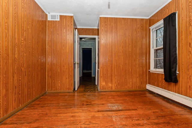 spare room with dark hardwood / wood-style flooring, baseboard heating, ornamental molding, and wood walls