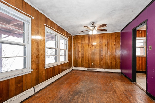 spare room with a baseboard radiator, dark hardwood / wood-style floors, wooden walls, and ceiling fan