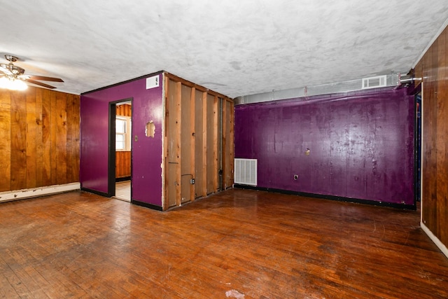 unfurnished room featuring baseboard heating, wooden walls, dark wood-type flooring, and a textured ceiling