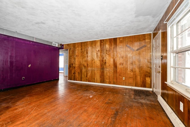 unfurnished room featuring dark hardwood / wood-style floors, wood walls, and a baseboard heating unit