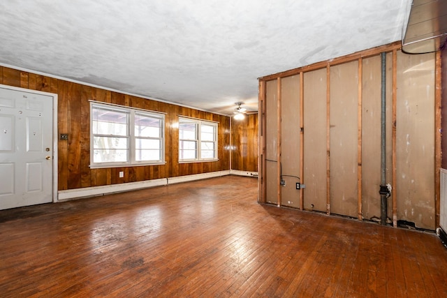 unfurnished living room with ceiling fan, hardwood / wood-style floors, wood walls, and a baseboard heating unit